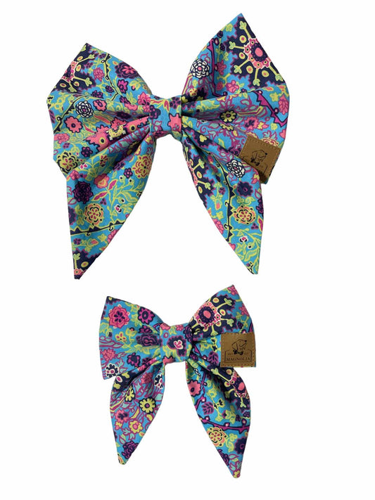 his beautiful accessory features an enchanting floral pattern with an array of pinks, blues, greens, and purples on a soft fabric background