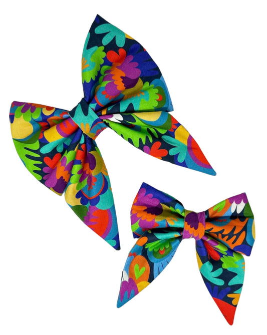 This cheerful and modern dog bow features a bold palette of purples, aquas, blues, reds, greens, and yellows on a navy background.