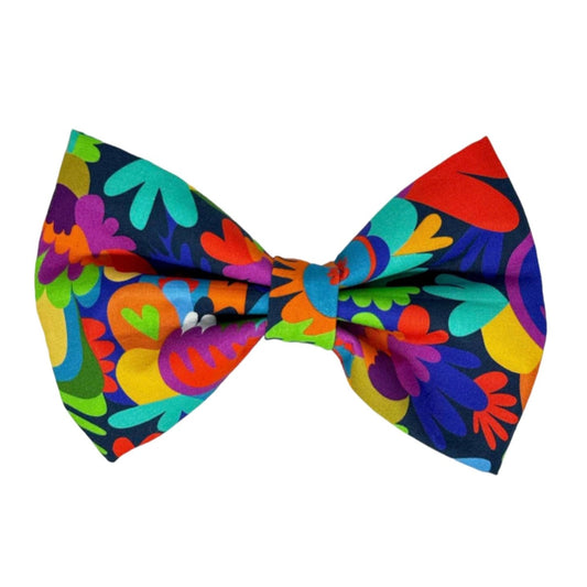 This cheerful and modern dog bow tie features a bold palette of purples, aquas, blues, reds, greens, and yellows on a navy background.