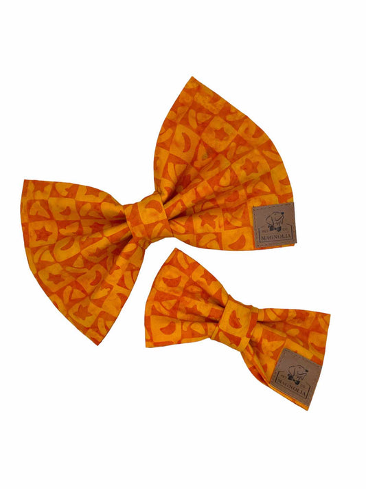 Crafted in a vibrant, eye-catching bright orange, this bow features an intricate pattern of checkered boxes, each adorned with whimsical stars and charming witches hats