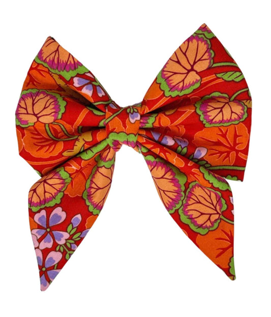 This lovely dog bow features a beautifully illustrated garden in shades of red, green, pink, and purple on a orange background by Magnolia Pet Company.