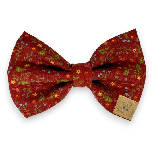 Crafted with meticulous attention to detail, this exquisite dog bow tie features a warm rust color as its base, adorned with delicate petite flowers in cheerful shades of yellow, blue, and red