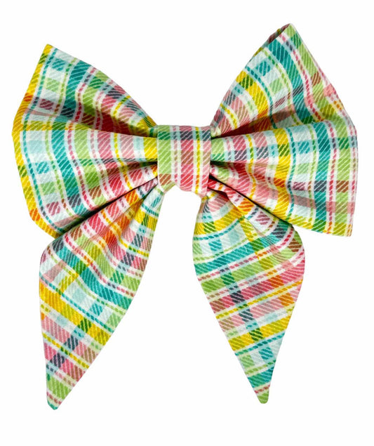 This timeless dog bow features a charming plaid pattern in pastel hues of pink, aqua, green, and yellow, set against a crisp white background by Magnolia Pet Company