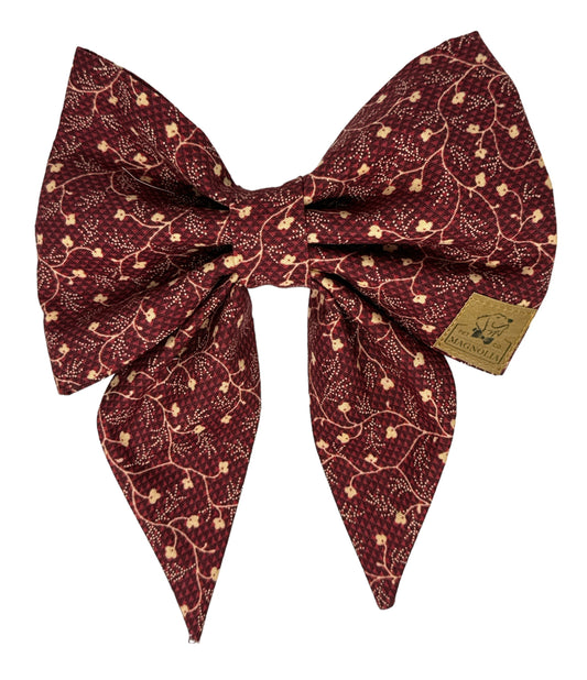 This sophisticated dog bow features a rich maroon fabric adorned with delicate off-white floral vine patterns that weave gracefully throughout the fabric