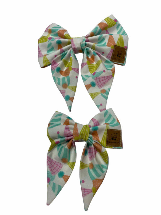 Our Birthday Bash dog bow features party hats with various hues of aqua, pink and lime green.