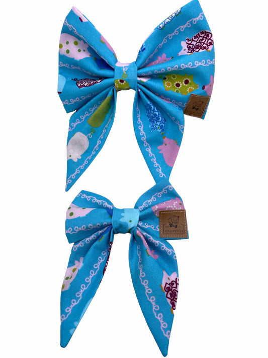 This adorable accessory features a vibrant blue fabric adorned with whimsically decorated pigs in a variety of cheerful colors