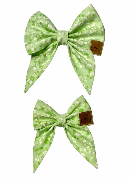 This elegant accessory features a light green fabric adorned with delicate white florals and rich dark green foliage.