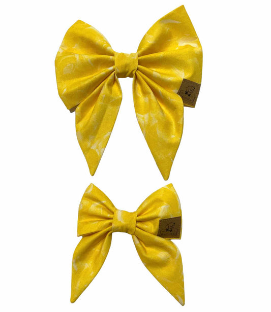 his enchanting bow is crafted from vibrant yellow fabric, adorned with elegant white feather wisps that add a touch of whimsy and grace.