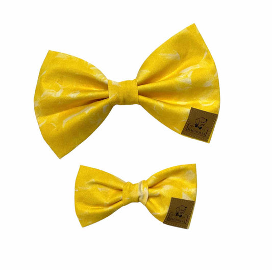 This enchanting bow is crafted from vibrant yellow fabric, adorned with elegant white feather wisps that add a touch of whimsy and grace