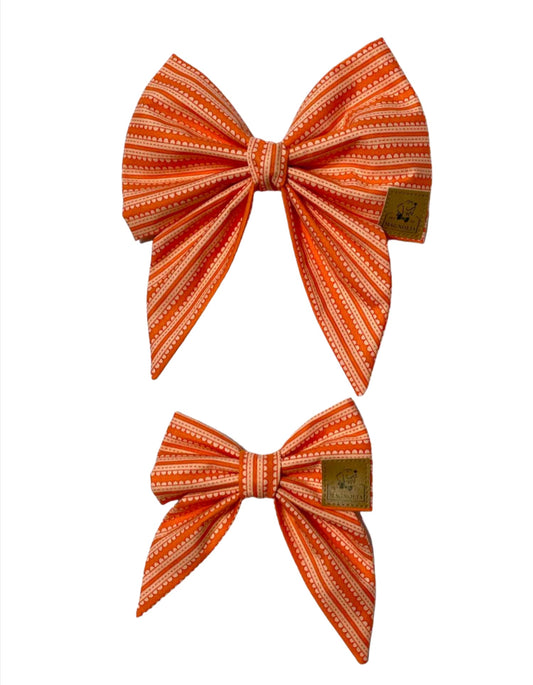 This delightful bow features an eye-catching pattern of white and orange stripes, perfect for adding a pop of color to any occasion