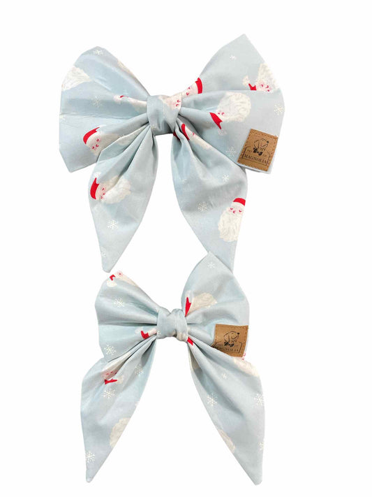 Celebrate the holiday season in style with our adorable dog bow featuring a jolly Santa  face on a light blue fabric background.