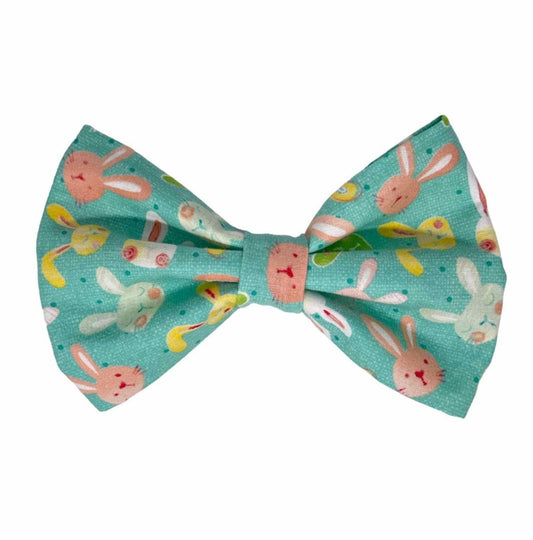 Hop into Spring with our delightful Bunny Hop Dog Bow Tie – the perfect accessory to add a touch of whimsy and cheer to your pet's ensemble!  Featuring a charming print of cute illustrated bunny faces in tones of pink, yellow, green, and white on a soft pastel aqua background, this bow captures the essence of springtime joy. 
