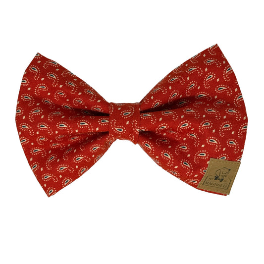 This exquisite dog bow tie features a rich crimson backdrop adorned with a delicate paisley design in shades of red, beige, and blue.