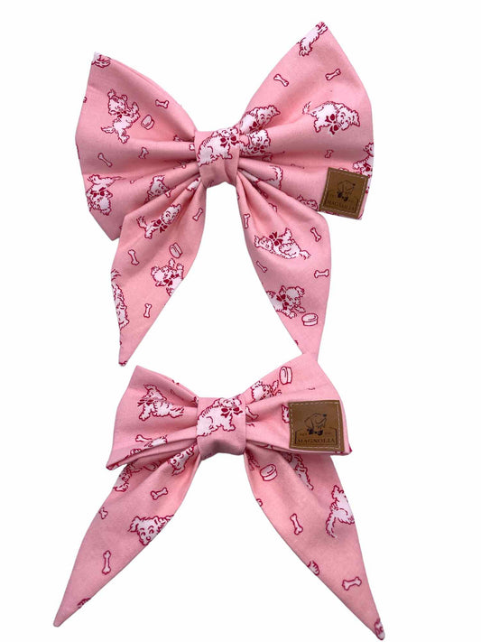 This charming accessory features a soft pink background, providing a delicate and stylish look. Each bow is adorned with a playful white dog design, beautifully outlined in hot pink, giving it a delightful pop of color. The pattern is completed with cute little dog bowls and bones